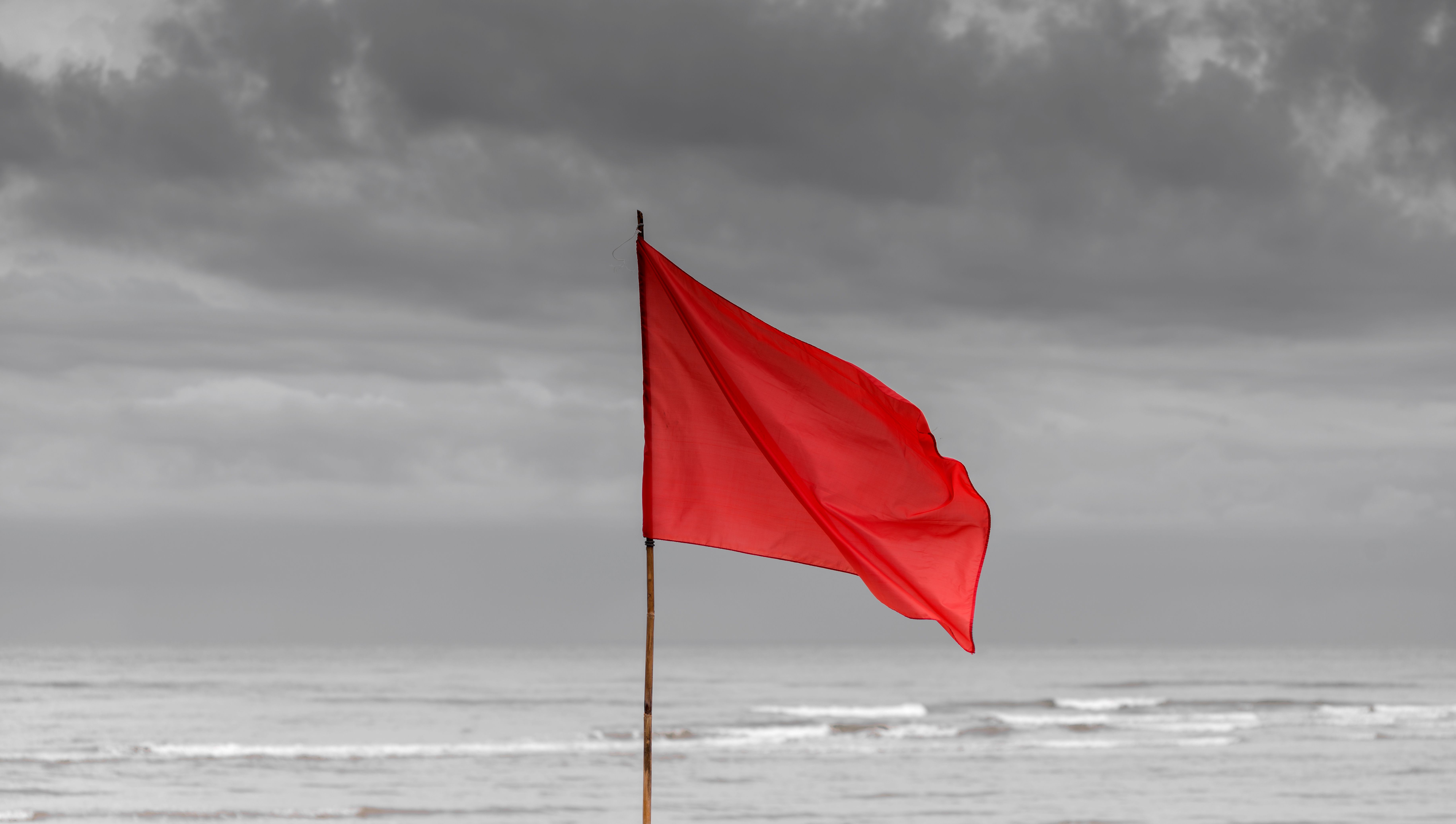 A bright red warning flag waving against a grey, stormy sky, symbolizing the critical warning signs and red flags patients must watch out for before aesthetic surgery.